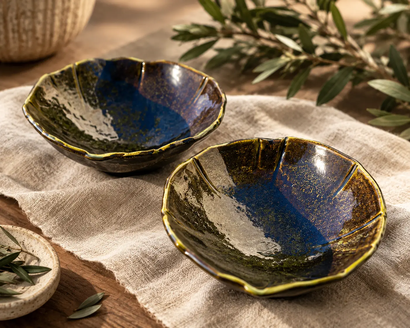 Two sculptural blue and green glazed ceramic bowls on cream linen